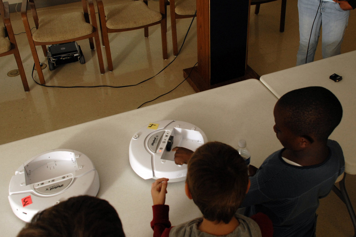 Elementary school students look at small round robots